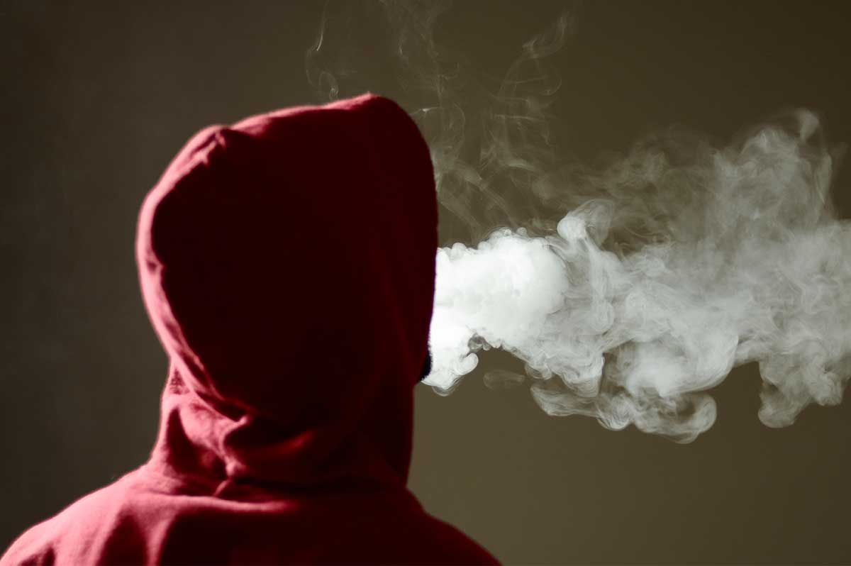 Youth in hoodie blowing vape smoke