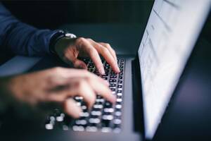 Man's hands typing on keyboard in dark room