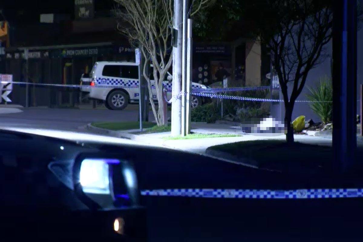 A dark street roped off by with police tape. A police car can be seen and a part of the image is pixelated