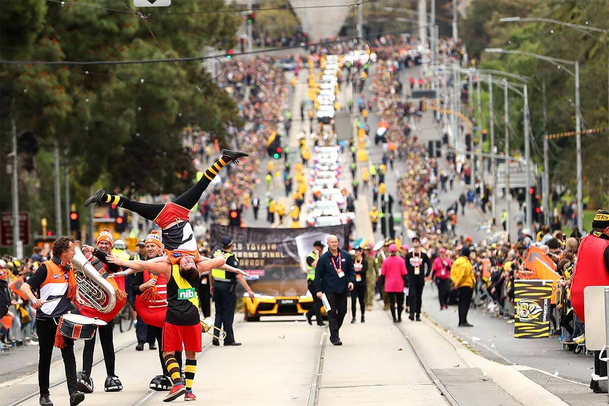 A parade travelling through Melbourne's CBD, there are banners and people dressed in Richmond and GWS colours
