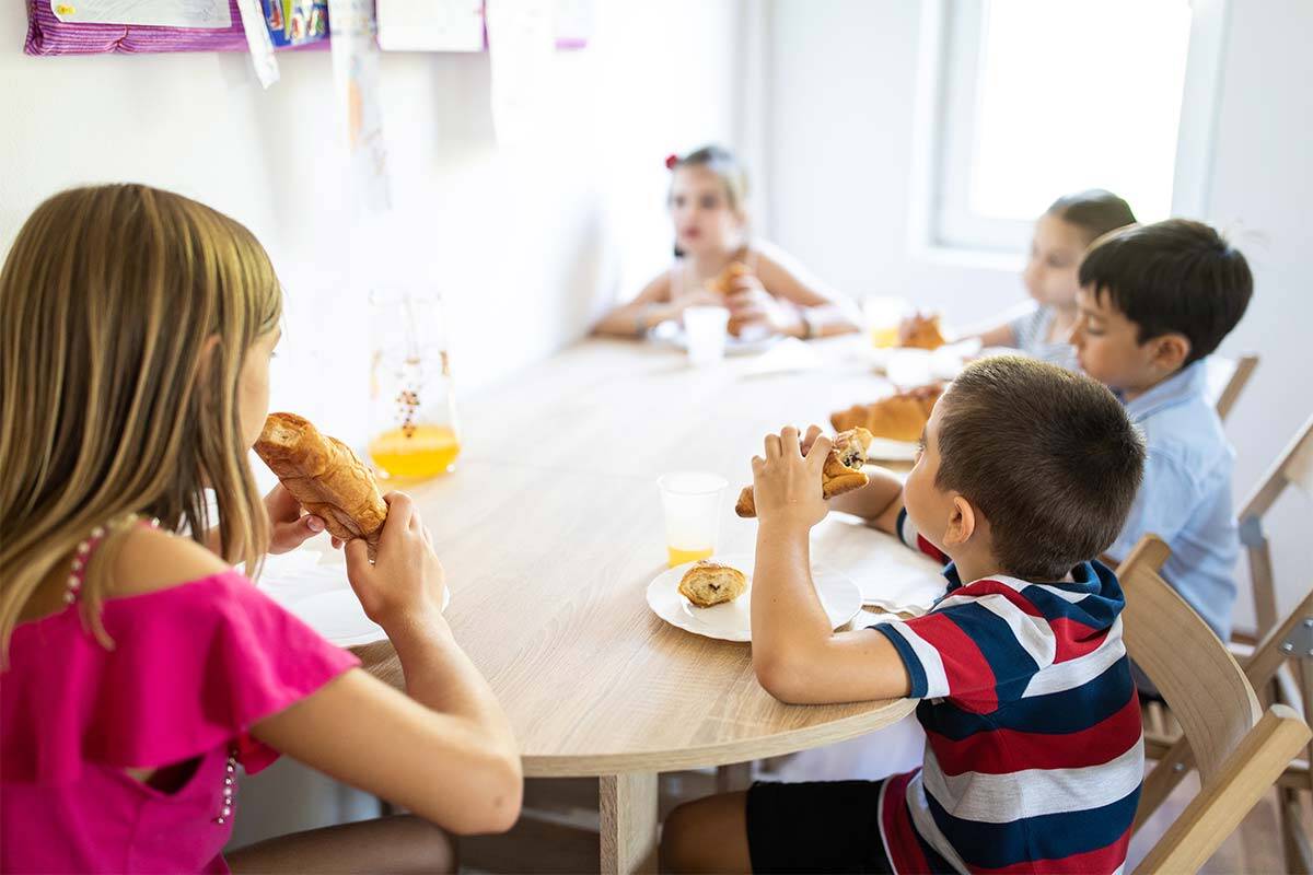 Five children sit at a table eating croissants